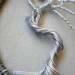 Detailed wire art featues a silver tree with twisted roots and branches inside a circular rustic frame extreme cloesup